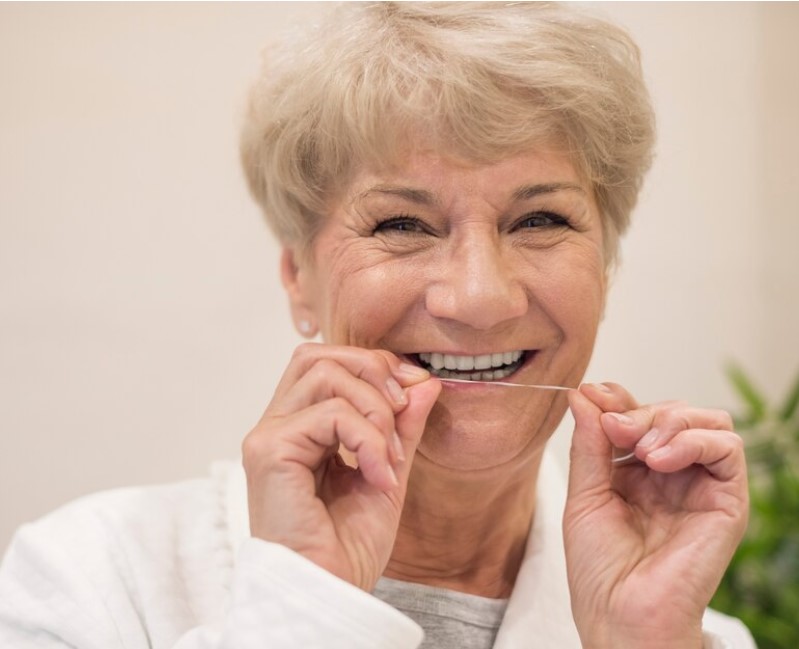 Mujer sonriendo mientras se pasa el hilo dental