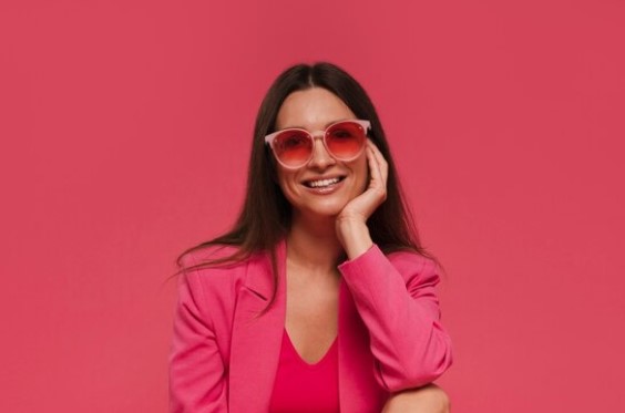 Mujer en fondo rosa con vestimenta rosa del mismo color, gafas rosas y sonriendo hacia la cámara