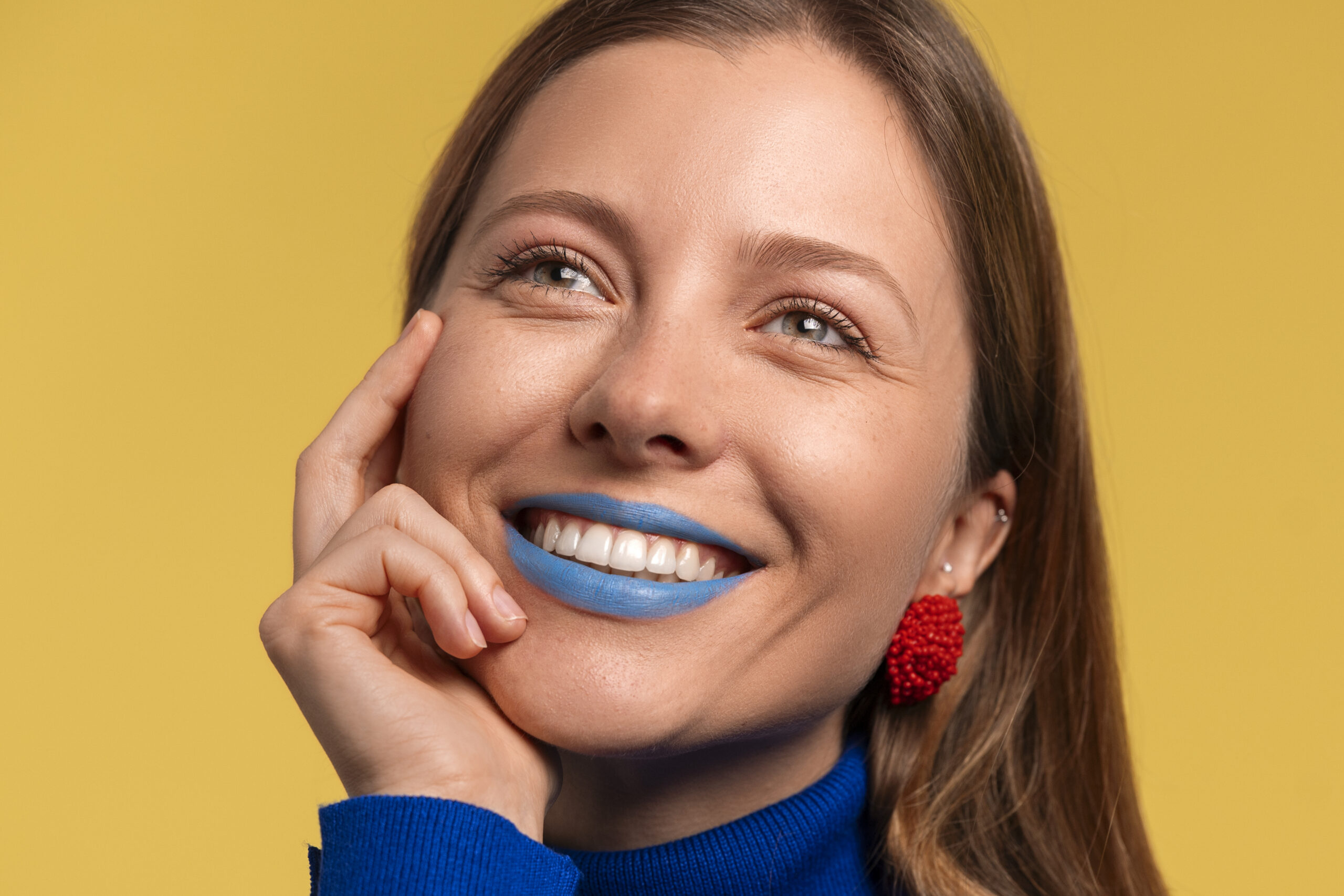 Mujer con labios pintados de azul, se toca la cara mientras sonrie