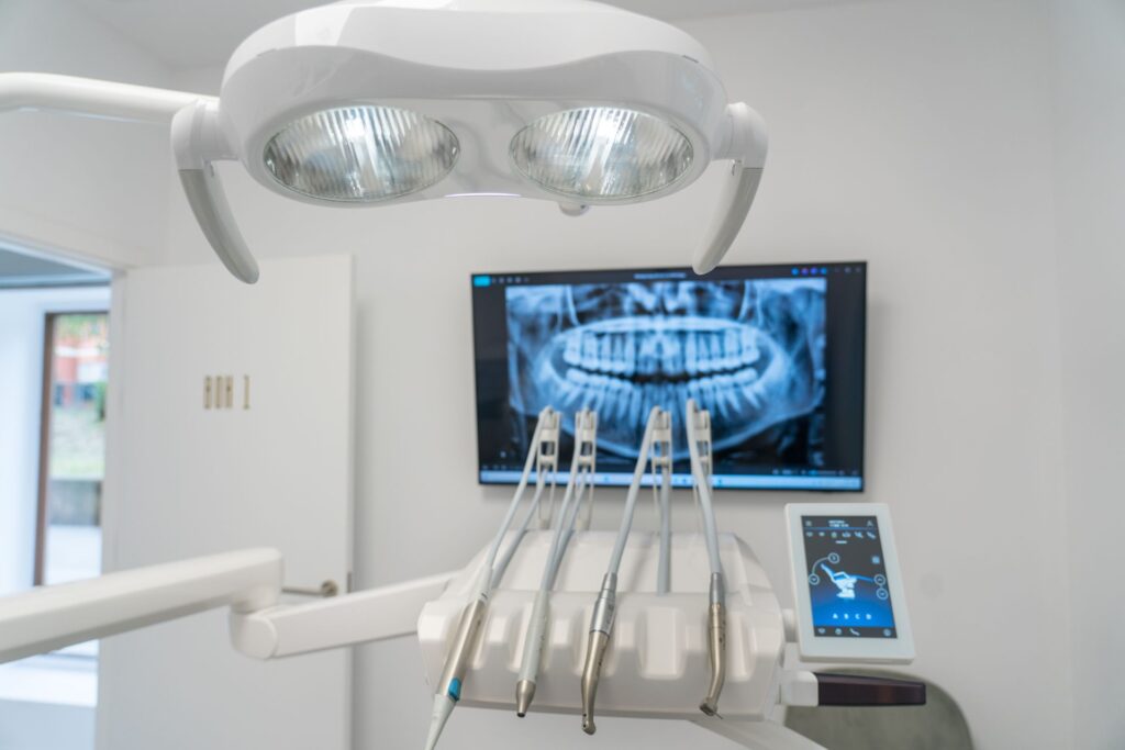 Silla dental con equipo en el fondo, mientras un dentista examina los dientes de una paciente.