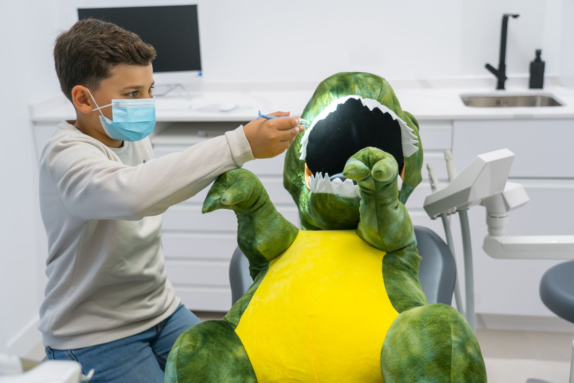 Niño en una consulta de dentista jugando a los dentistas con un dinosaurio de peluche